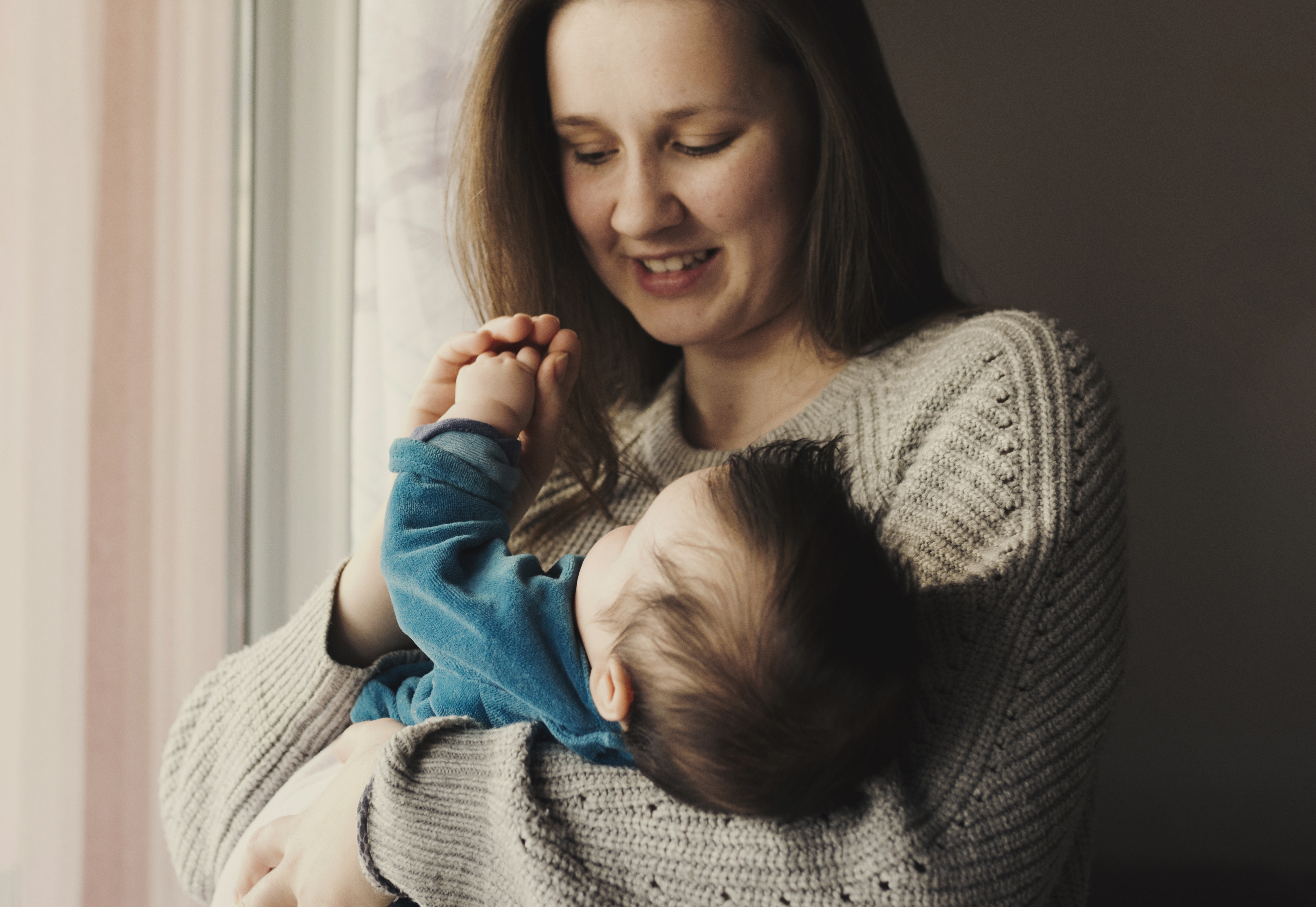 Madre sonriente y relajada junto a su bebé en un entorno doméstico, representando la etapa postparto y la importancia del autocuidado para la recuperación del bienestar físico tras el embarazo.